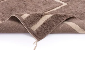 A luxurious hand-knotted brown rug with a textured surface and beige striped edges is elegantly displayed on a white surface.