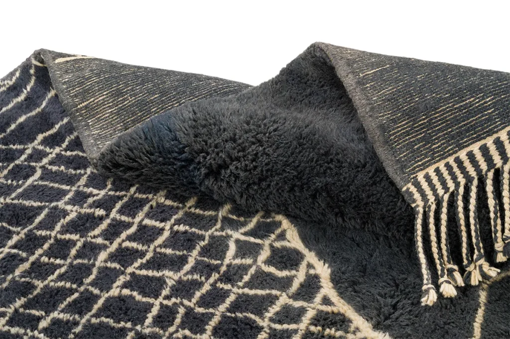 A luxurious black and white patterned rug, hand-knotted with a unique design and tasseled edge, exudes the elegance of a Moroccan rug.