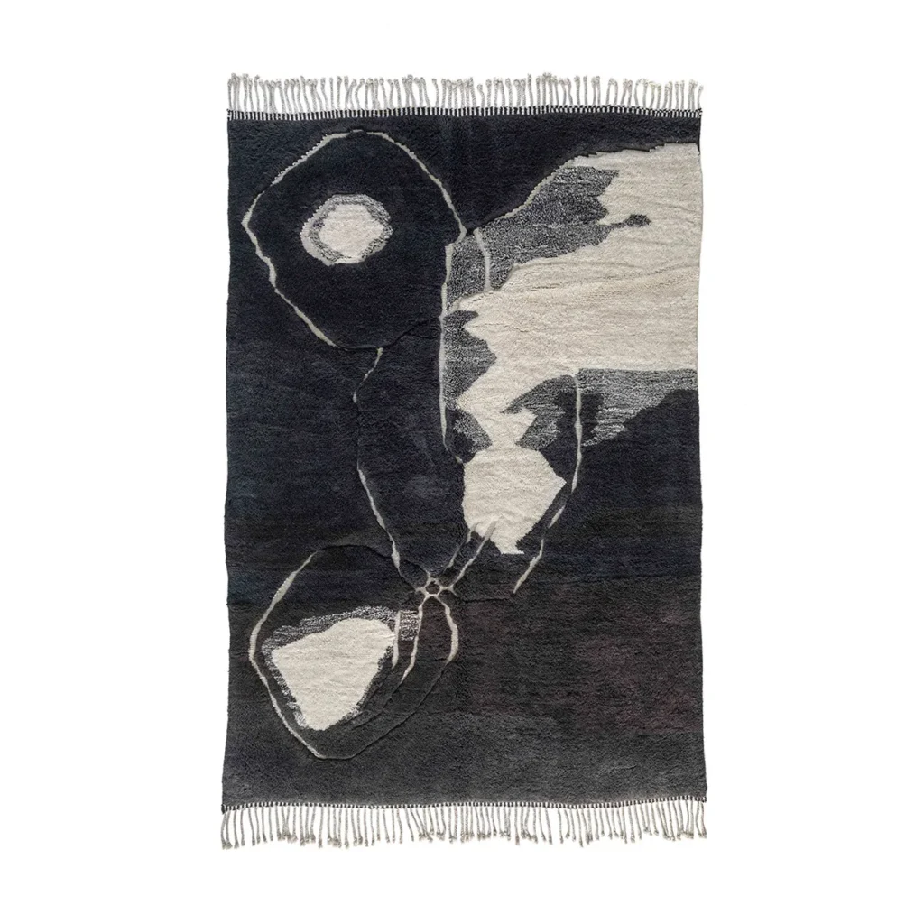 An artisanal black and white rug with fringed edges, showcasing hand-knotted, geometric, and organic shapes in dark and light shades.