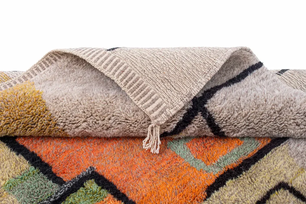 This vibrant, hand-knotted rug features bold geometric patterns in orange, green, and black. The textured reverse side highlights its artisanal craftsmanship, reminiscent of authentic Moroccan rugs.
