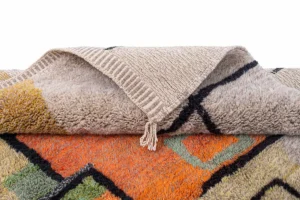This vibrant, hand-knotted rug features bold geometric patterns in orange, green, and black. The textured reverse side highlights its artisanal craftsmanship, reminiscent of authentic Moroccan rugs.
