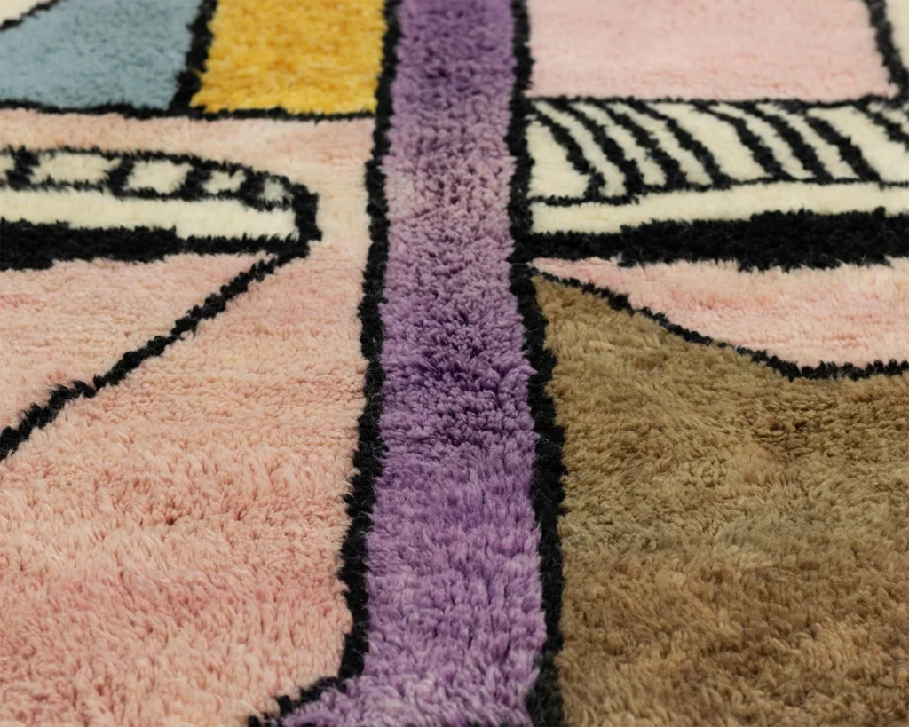 Experience the artistry of Authentic Moroccan Rugs in this close-up shot of a textured, hand-knotted rug. The vivid abstract patterns in pink, purple, brown, yellow, and blue shades capture an exquisite blend of tradition and contemporary design.