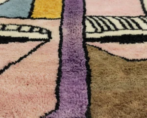 Experience the artistry of Authentic Moroccan Rugs in this close-up shot of a textured, hand-knotted rug. The vivid abstract patterns in pink, purple, brown, yellow, and blue shades capture an exquisite blend of tradition and contemporary design.