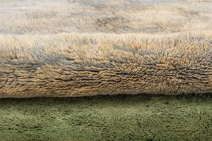 A close-up view showcases two stacked cozy textiles, with the top in a light beige tone and the bottom in a green shade.
