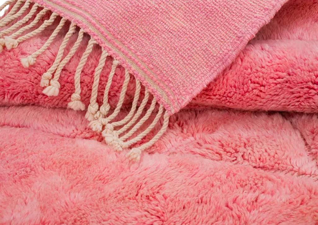 A pink woven tapestry with tassels adorns a plush, textured pink fabric, echoing the timeless elegance of hand-knotted rugs.