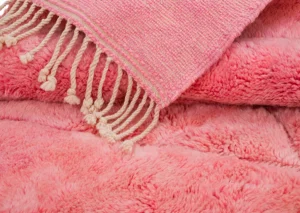 A pink woven tapestry with tassels adorns a plush, textured pink fabric, echoing the timeless elegance of hand-knotted rugs.