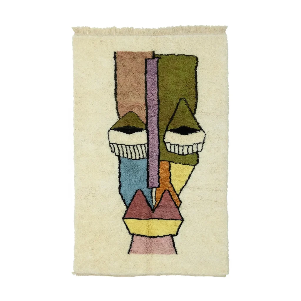 A hand-knotted rectangular rug with a colorful abstract face design featuring geometric shapes on a beige background.