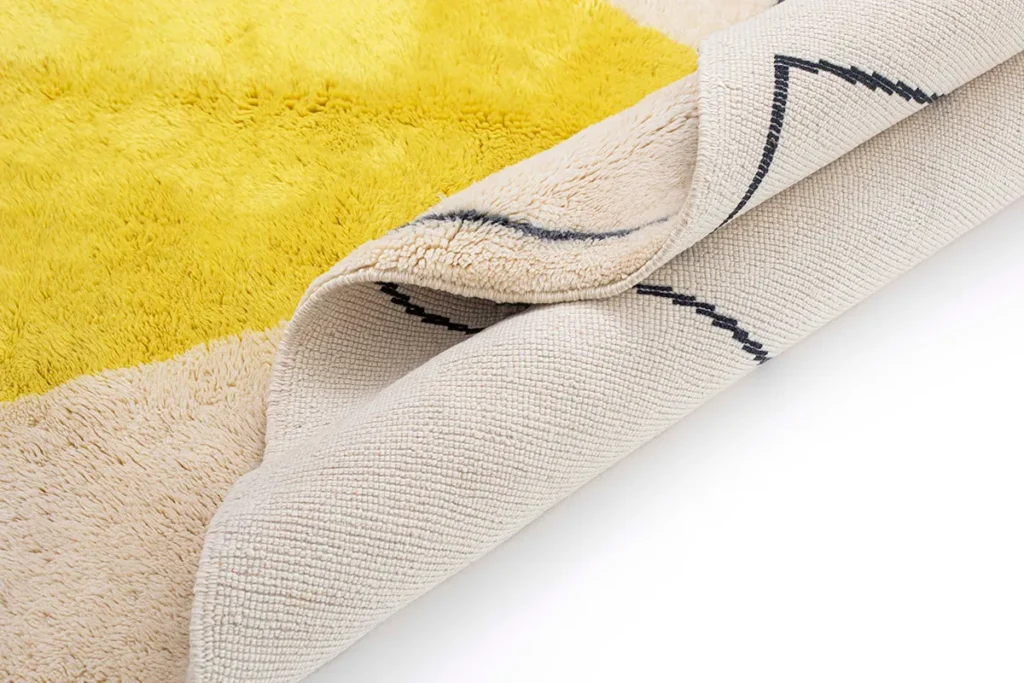 A luxurious yellow and beige fluffy rug is elegantly folded to reveal its textured backside, highlighting the intricate pattern and materials.