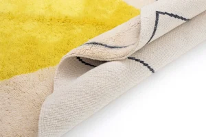 A luxurious yellow and beige fluffy rug is elegantly folded to reveal its textured backside, highlighting the intricate pattern and materials.