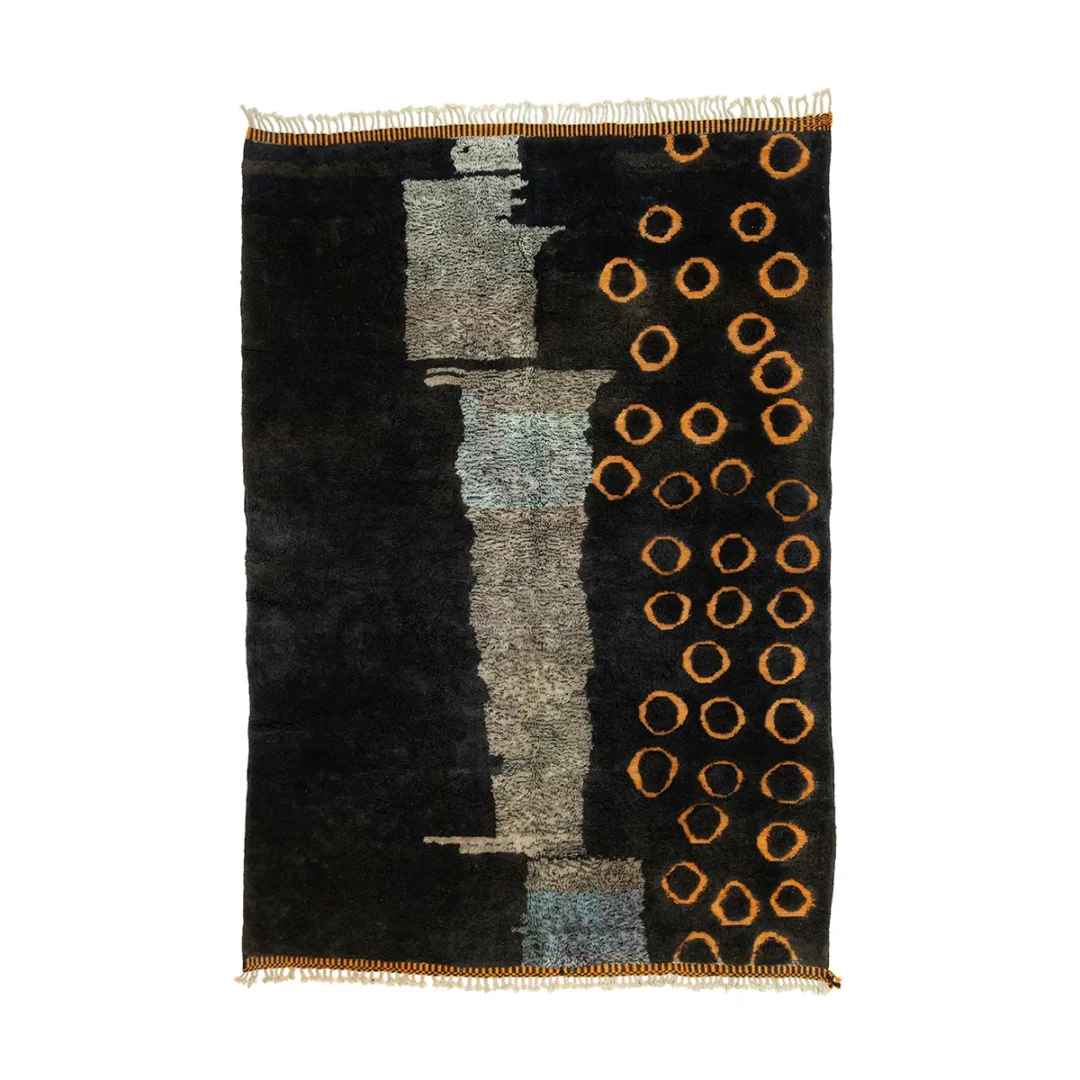 Dark Moroccan rug displaying an abstract design with patches of grey and teal, complemented by orange circular patterns on one side.