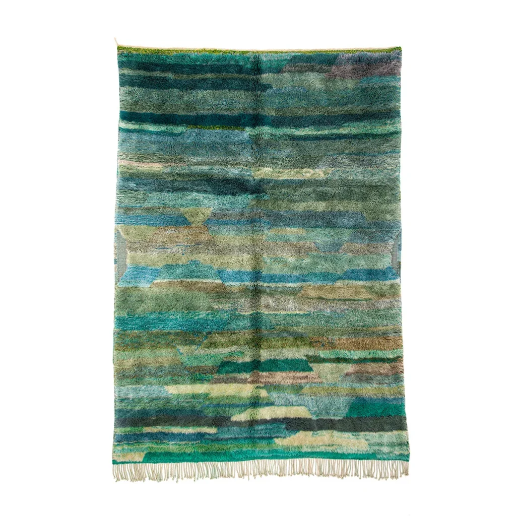 A luxurious, rectangular, hand-knotted rug showcases a multicolored geometric pattern in shades of green, blue, and beige, accented with short fringes along the bottom edge.