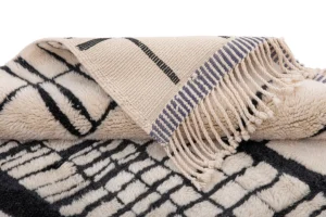 A luxurious cream and black Moroccan rug featuring a geometric design and elegant fringe detailing on the edges. This hand-knotted masterpiece adds a touch of sophistication to any space.
