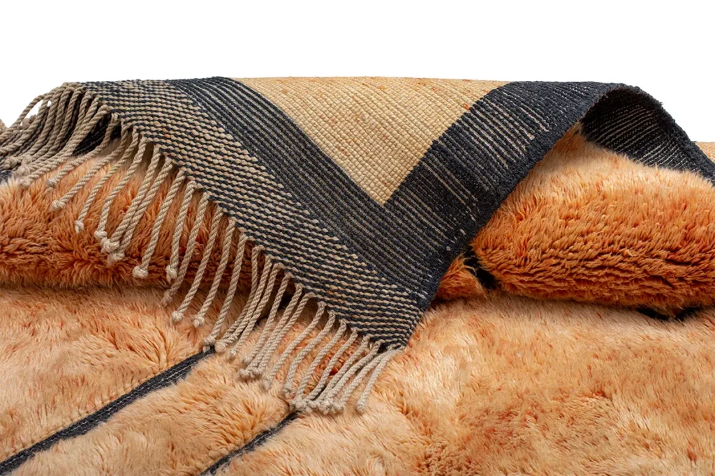 A luxurious, brown and beige woven rug with black stripes and fringes is artfully draped, showcasing its exquisite design.