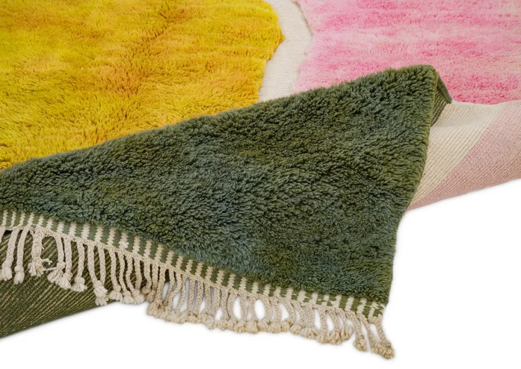 A luxurious, multicolored, fluffy rug showcases hand-knotted craftsmanship. It features vibrant yellow, pink, and green sections with fringed edges and is shown partially folded to emphasize its rich texture and striking colors.