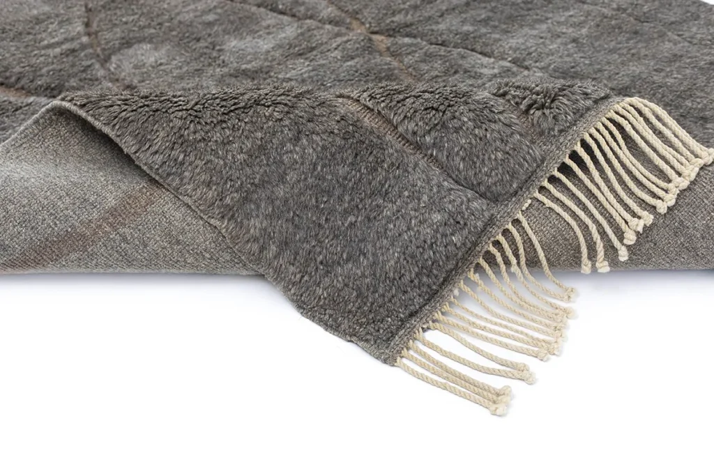 A folded, soft gray textile with fringed edges showcases artisanal craftsmanship.