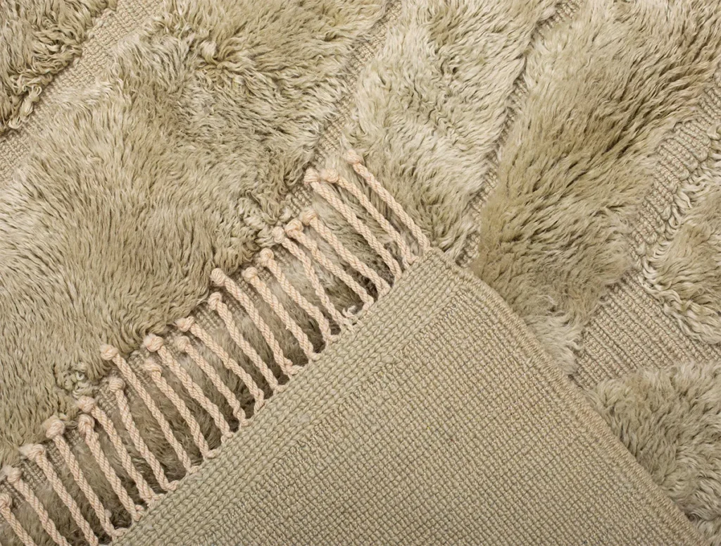 Close-up of a beige textured Moroccan rug with a fringe, featuring a combination of shaggy and woven patterns.