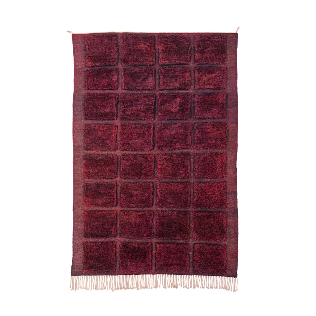 This luxurious, hand-knotted rug features a rectangular design in textured red and black. The eye-catching grid pattern of large squares is beautifully finished with fringes at the bottom, making it an elegant addition to any room.