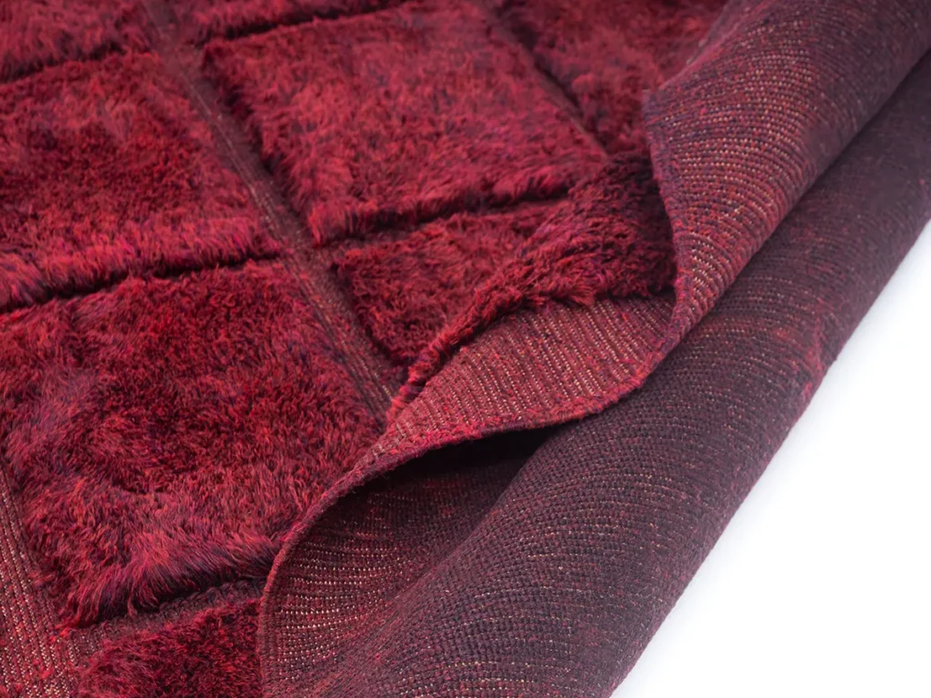 This captivating close-up showcases the intricate details of a luxurious red shaggy rug with a grid pattern, partially folded to reveal its expertly hand-knotted underside.