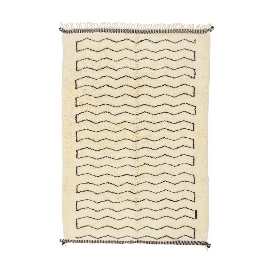 This luxury rug is rectangular and beige, featuring hand-knotted black zigzag patterns running horizontally. The fringed edges add a touch of elegance.