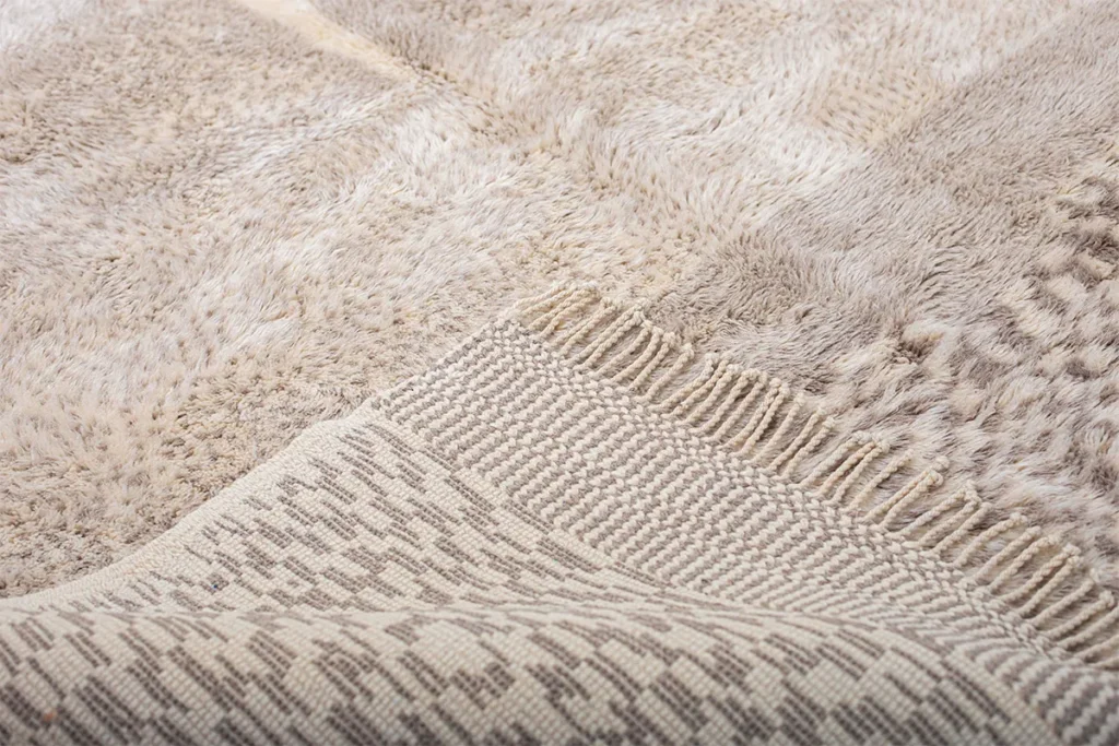 Close-up of a beige patterned Moroccan rug with various textures. The fabric showcases geometric designs and a blend of woven and plush materials, epitomizing luxury.