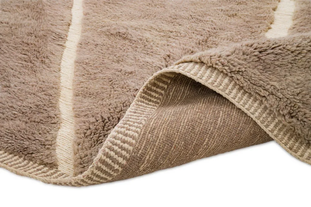 Close-up of a beige and brown striped luxury rug corner, showcasing its soft, fluffy texture on top and intricately woven underside.