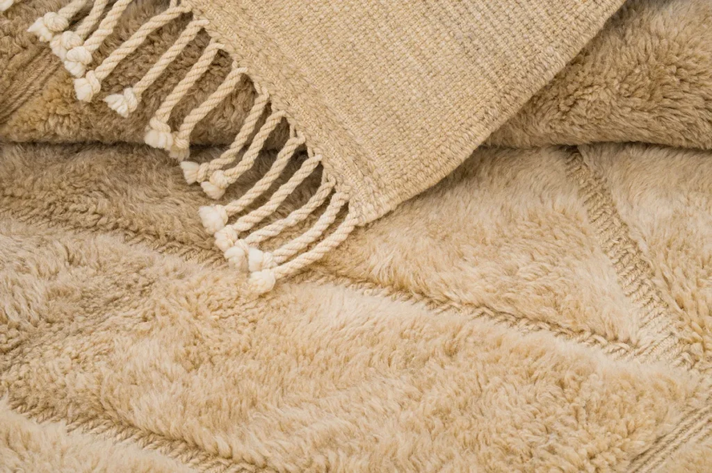 Close-up of an authentic Moroccan rug with fringe resting on a fluffy, soft beige surface.