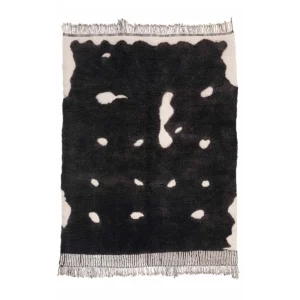 An artisanal rectangular rug with a black abstract pattern featuring irregular white spots, framed by fringed edges, reminiscent of authentic Moroccan rugs.