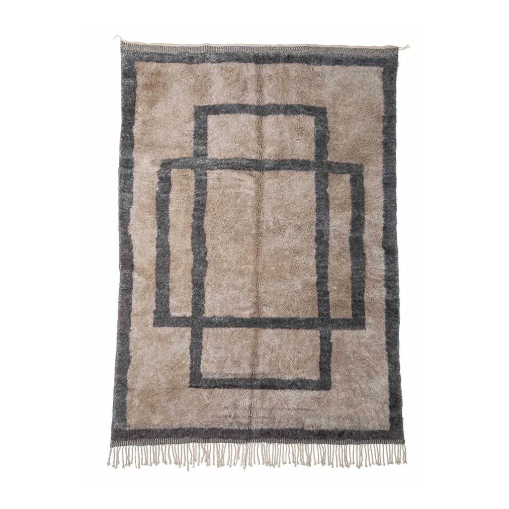 An artisanal rug in beige and gray features a geometric pattern of overlapping rectangles, complemented by fringe on the edges, all set against a white background.