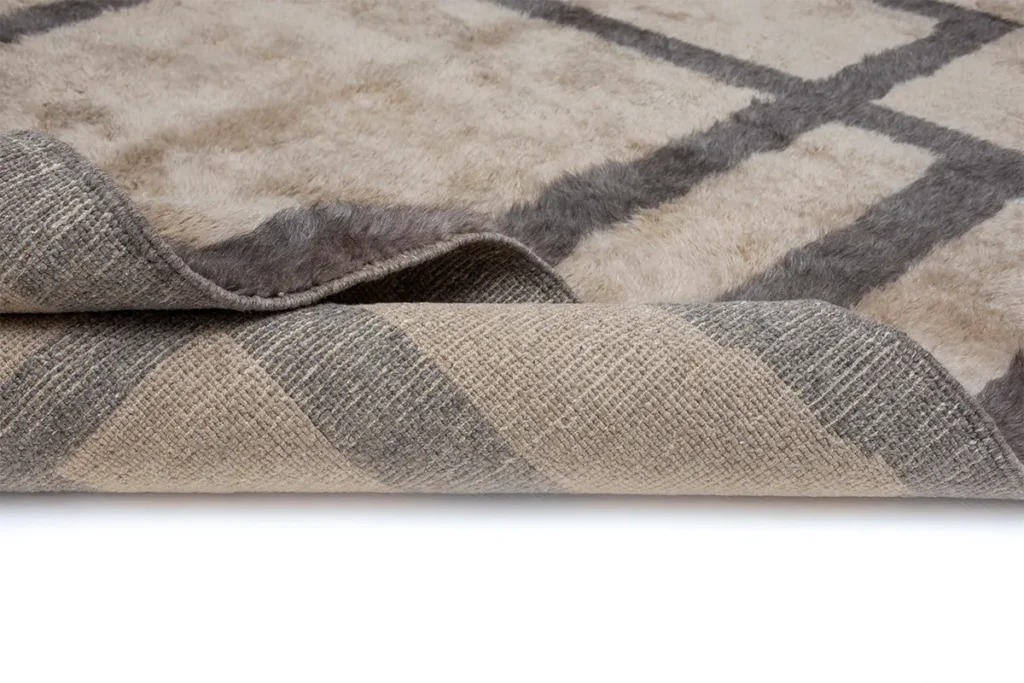 A rolled-up section of an artisanal, beige and gray checkered rug, revealing its textured underside, is displayed against a plain white background.