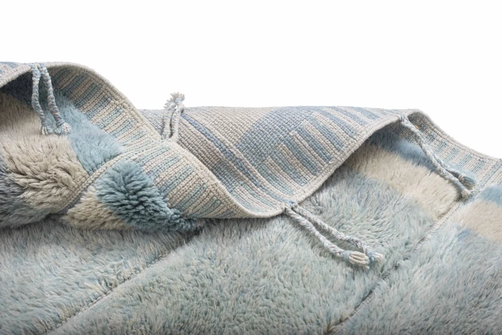 A folded, light blue and beige striped textured fabric with tassels against a white background. Its elegant blend of colors and delicate detailing adds a touch of sophistication to any room.