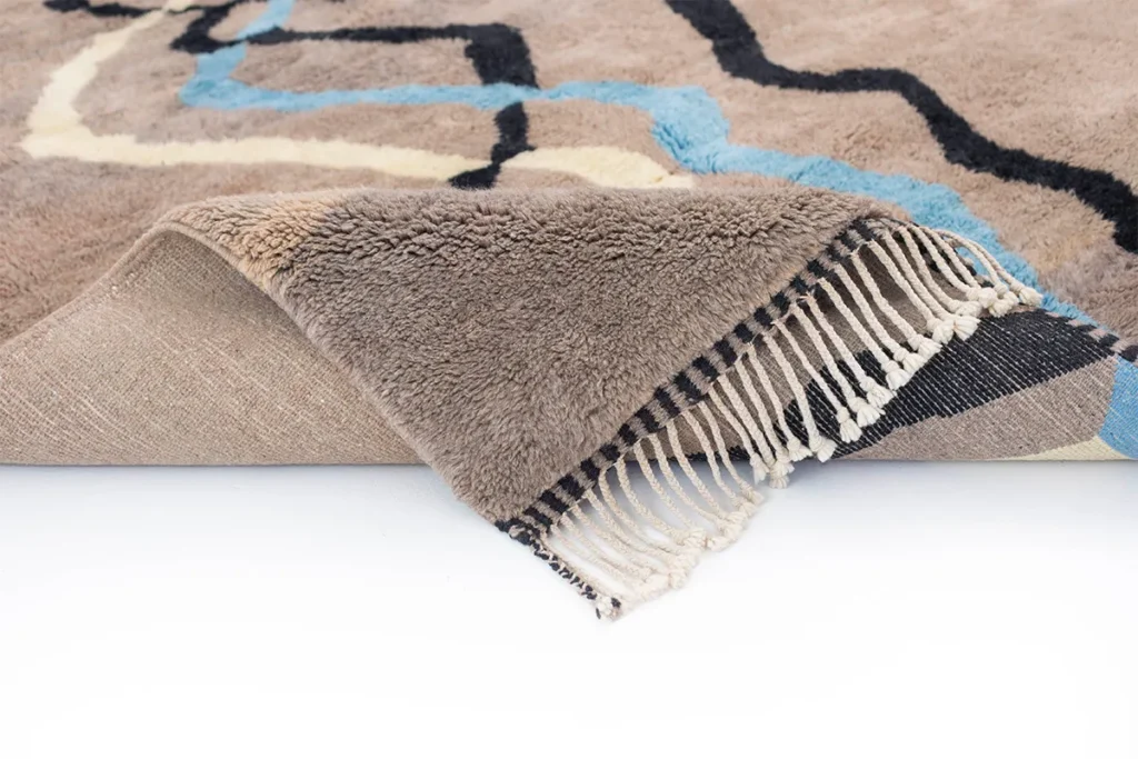 An artisanal rug with abstract patterns is partially turned up, revealing a striped underside and fringed edges.
