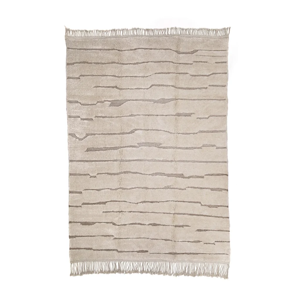 Discover a beige artisanal rug, hand-knotted with delicate precision. Its pattern of irregular horizontal lines and fringed edges adds a touch of elegance to any space, embodying the essence of authentic Moroccan rugs.