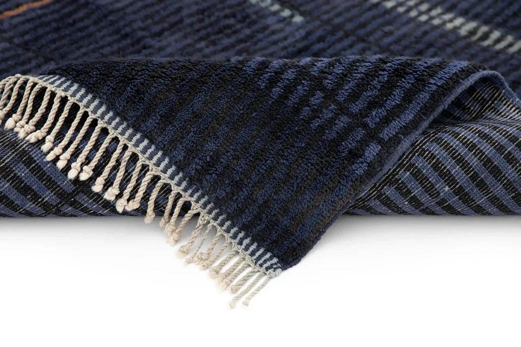A luxurious Moroccan rug in dark blue checkered fabric with white fringed edges lies partially folded on a flat surface.