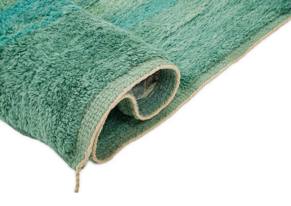 This close-up showcases a luxurious rolled green textured rug with a beige trim, set against a white background.