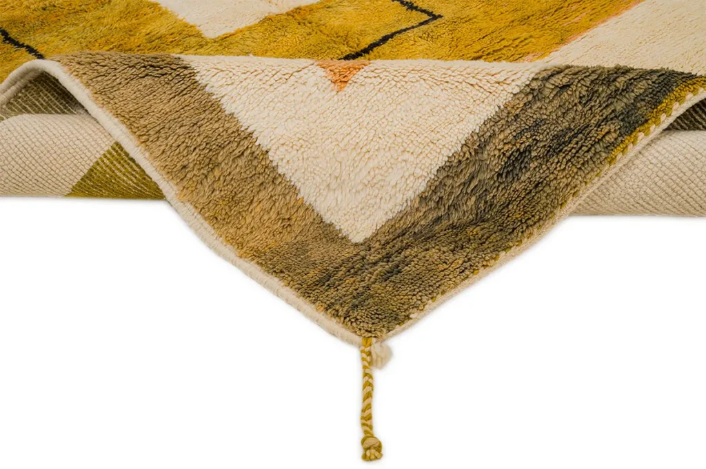Close-up of a luxurious, hand-knotted rug showcasing a geometric pattern and knotted tassel. The elegant design features shades of yellow, white, and brown, reminiscent of Moroccan artistry.