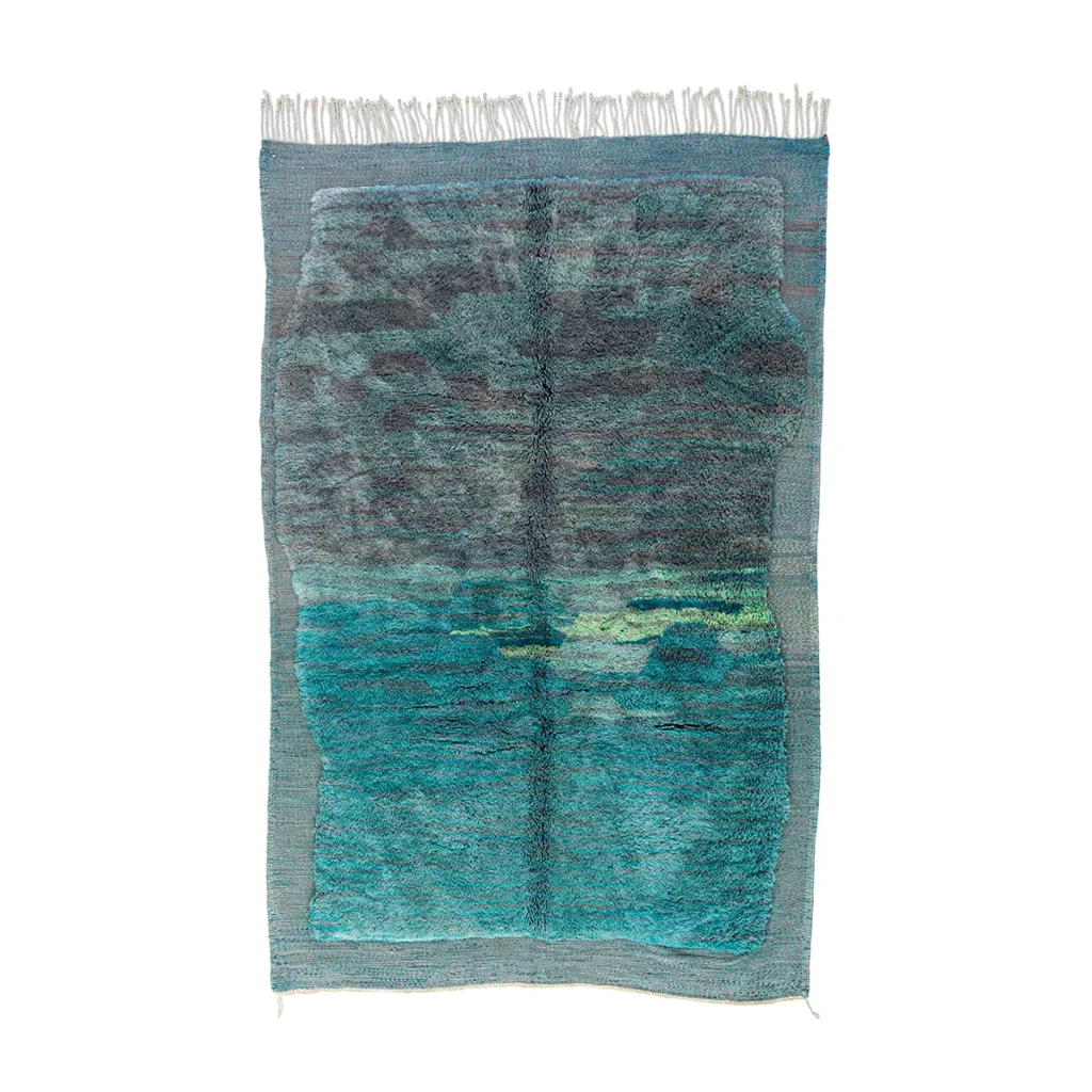 A luxurious rectangular woven tapestry with fringe, this exquisite piece showcases a landscape featuring a cloudy sky and a body of water in shades of teal, green, and gray.