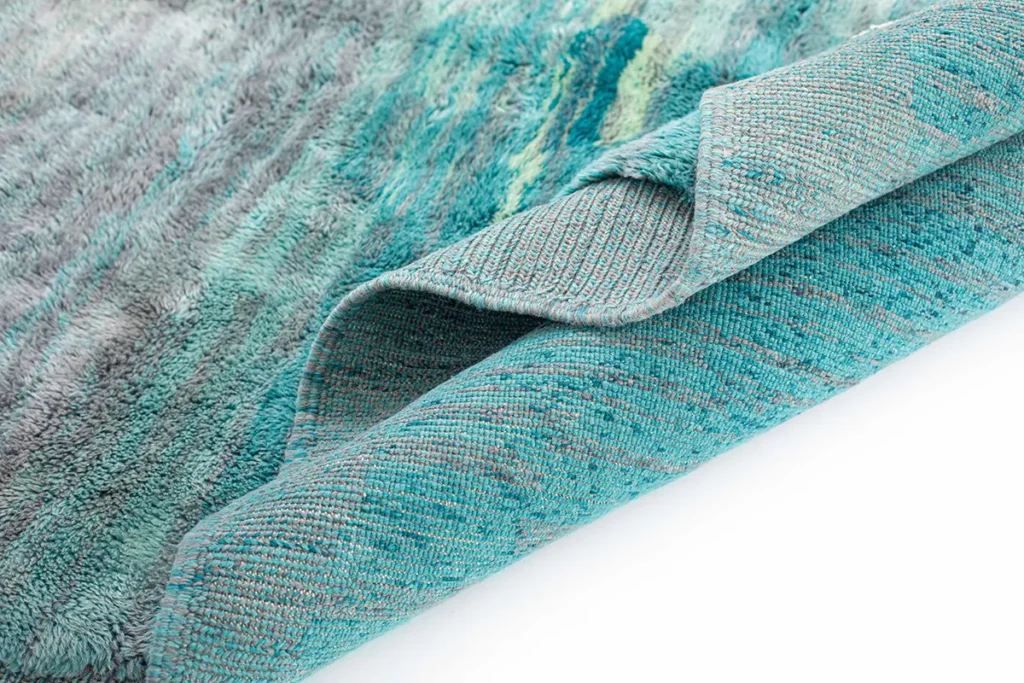 Close-up of a luxurious blue and gray textured rug with a visible underside, showcasing its hand-knotted pattern.