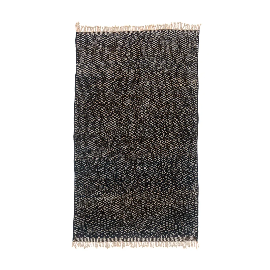 An artisanal rug featuring a black and beige woven textile showcases small dot patterns and fringe detail on its shorter edges, reflecting the timeless elegance of authentic Moroccan craftsmanship.