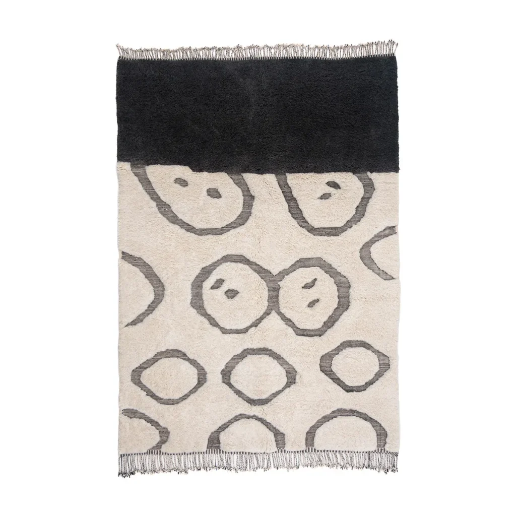 Discover the elegance of a hand-knotted rectangular rug, showcasing a black section on top and a cream section below, adorned with a pattern of large black circles. Fringe detailing graces the edges for added charm.