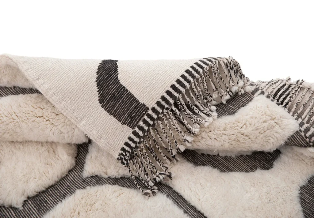 A close-up of a hand-knotted fabric with black and white geometric patterns and fringed edges, resembling authentic Moroccan rugs, showcased with artisanal precision.