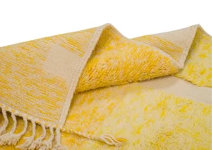 A folded luxury rug in yellow and beige, beautifully woven with fringed edges, showcasing a delightful blend of rough and smooth textures.
