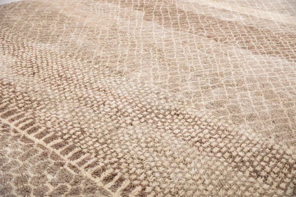 This hand-knotted beige rug features a textured design with various woven patterns, including small squares and grid-like designs, creating a layered appearance.