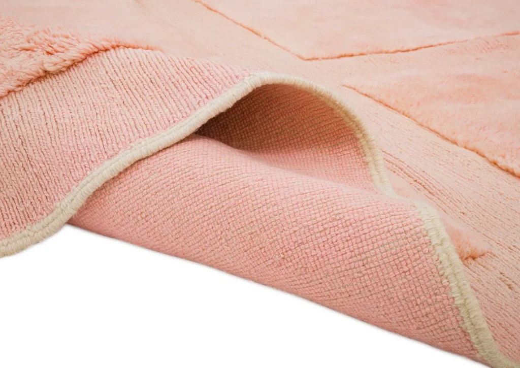 A close-up of a pink textured rug with a corner gently folded back reveals its soft, light-colored underside, adding an inviting warmth to the room.