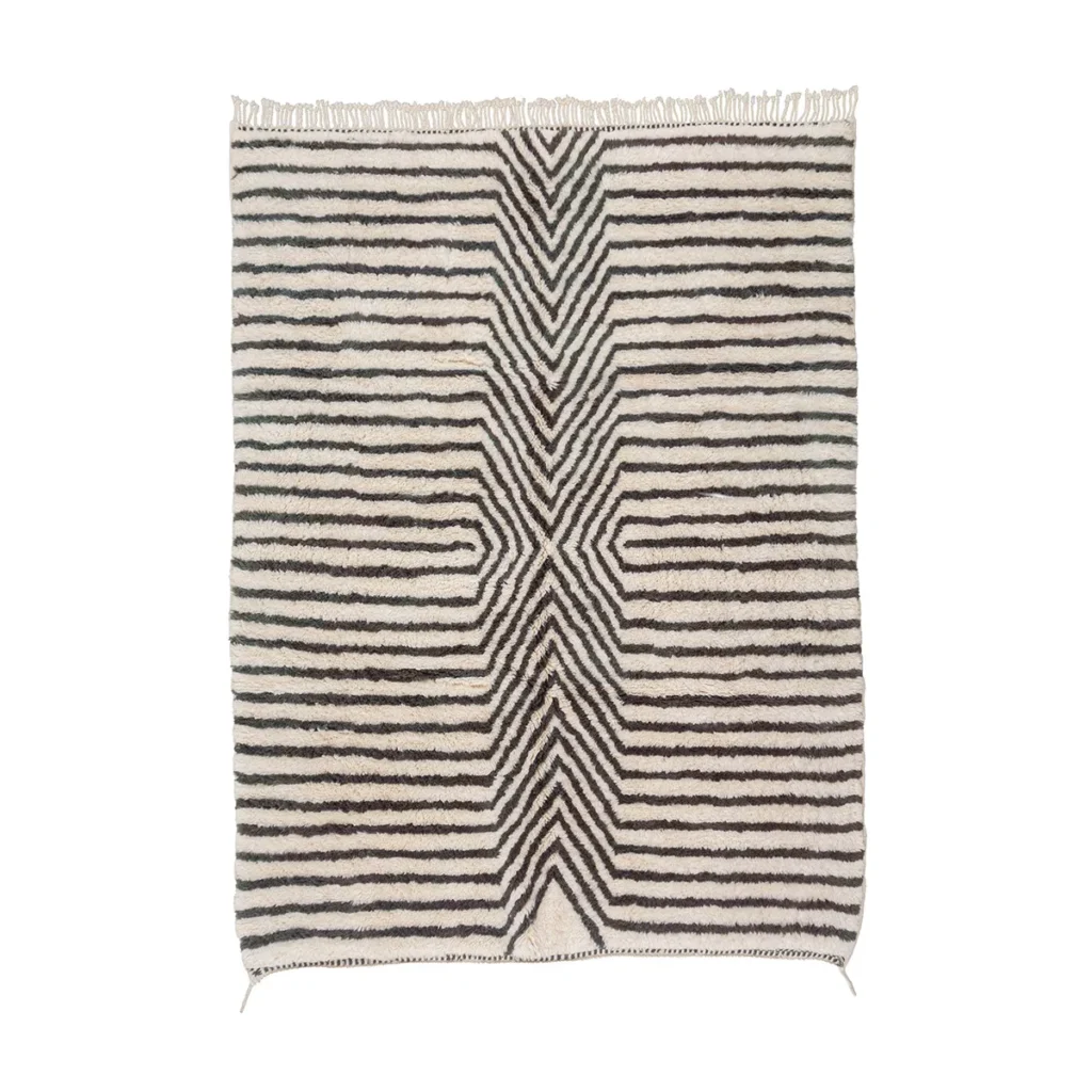 An artisanal rug with black and white striped geometric patterns showcases a symmetrical design converging toward the center, enhanced by fringe detailing. This hand-knotted piece embodies traditional craftsmanship and is sure to add elegance to any space.