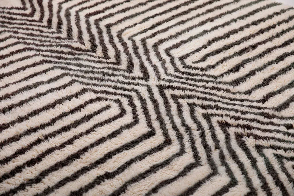 Close-up of a textured fabric featuring a black and white geometric zigzag pattern, reminiscent of an abstract maze. This design evokes the intricate details often found in artisanal rugs, showcasing the artistry behind hand-knotted creations.