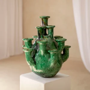 Green, multi-spouted ceramic vase with a glossy finish, displayed on a white pedestal against a blurred, neutral background.