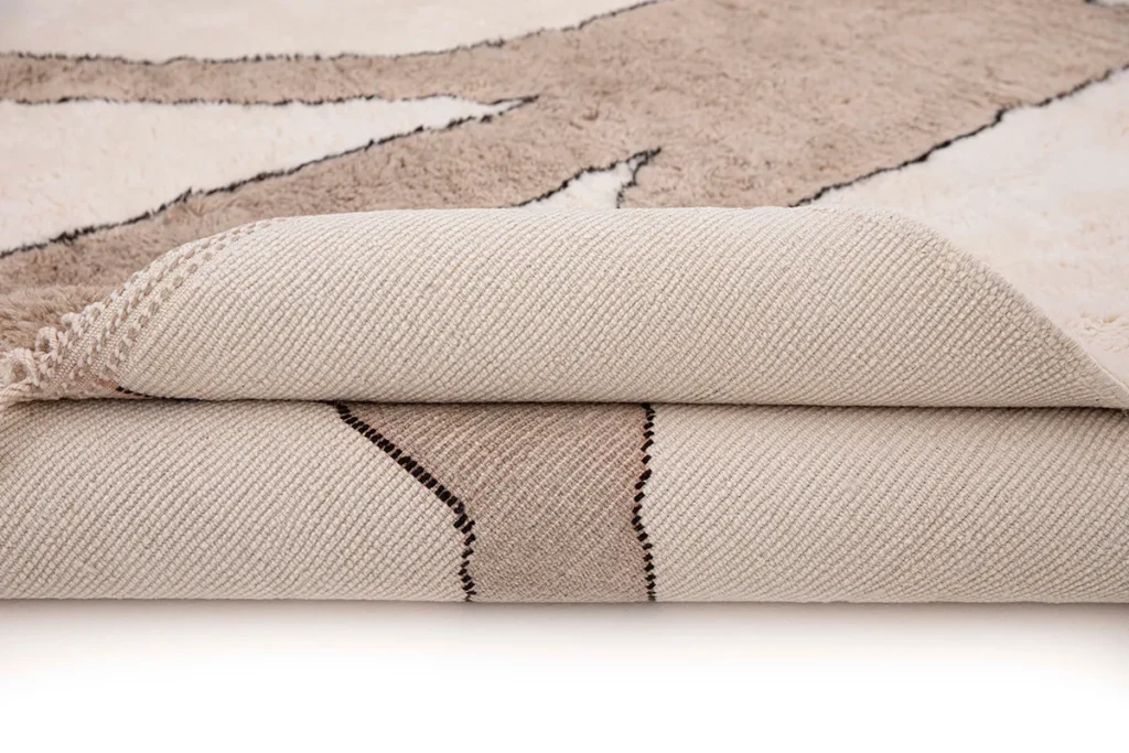 A close-up of a partially rolled beige and brown luxury rug with a geometric pattern, highlighting its intricate texture and design details.