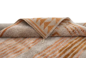A luxurious piece showcasing geometric designs in orange and beige, this item features a textured surface reminiscent of hand-knotted rugs.