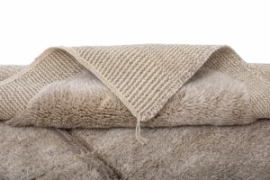 Close-up of a textured, hand-knotted rug with a woven pattern underneath, revealing its soft, luxurious surface.