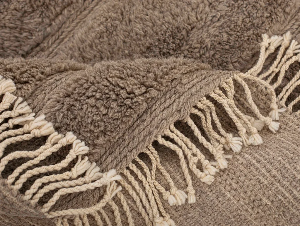 Close-up of a beige textured fabric with cream-colored fringe detailing, reminiscent of the intricate designs found in luxury rugs.